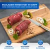 Two raw beef roulades secured with metal clips on a wooden cutting board, with ingredients like pickles, onions, parsley, and peppercorns scattered around. Produktbild-Vorschau