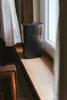 A black dehumidifier sits on a wooden windowsill next to a white curtain. Produktbild-Vorschau