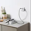 A smartwatch is charging on a stack of books on a desk, with a power adapter plugged into a wall socket. Náhled obrázku produktu