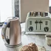 A toaster and a kettle are on a marble countertop, with bread and a cup of coffee. Voir les images du produit