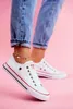 A person wearing jeans and white sneakers with an anklet, against a pink background. Voir les images du produit