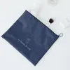 A navy blue cosmetic bag is laid flat on a white surface, with some cosmetic items visible around it. Anteprima dell’immagine prodotto