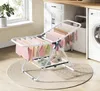 A small, foldable drying rack with clothes and shoes on it, placed on a rug in a laundry room setting. Produktbild-Vorschau