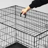 A hand is shown holding the handle of a black wire pet crate. Podgląd zdjęcia produktu