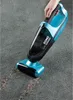 A hand is holding a blue and black handheld vacuum cleaner, cleaning a grey carpet. Produktbild-Vorschau