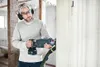 A man is using a reciprocating saw to cut a wall in a room under renovation. Voir les images du produit