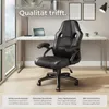 A black office chair is placed in front of a desk with a laptop and a lamp, near a large window. Produktbild-Vorschau