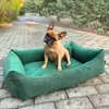 A French bulldog sits in a green dog bed outdoors on a paved walkway. Náhled obrázku produktu