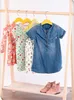 A wooden children's clothes rack with several dresses hanging on it and a pair of pink boots on the shelf below. Produktbild-Vorschau