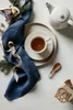A flat lay of a tea set with a blue napkin, a decorative bird, and a gift box. Produktbild-Vorschau