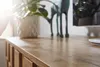 A close-up view of a wooden surface, likely a tabletop or dresser, with a plant in a pot and a decorative deer figurine in the background. Produktbild-Vorschau