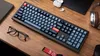A desk setup with a keyboard, glasses, headphones, and earbuds. Produktbild-Vorschau