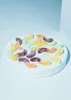 Gummy worms arranged on a white circular platform against a light blue background. Produktbild-Vorschau