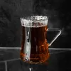 A close-up shot of a glass teacup filled with dark tea, set against a dark, textured background. Voir les images du produit
