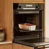 A loaf pan with food inside is placed on a rack inside an open oven, set within a modern kitchen. Voir les images du produit
