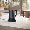 A black electric kettle sits on a marble countertop in a modern kitchen with large windows overlooking an outdoor space. Podgląd zdjęcia produktu