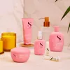 A collection of pink hair care products arranged on a marble-like surface, with a candle and greenery in the background. Voir les images du produit