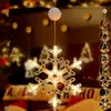 A snowflake-shaped LED light decoration hangs in a dimly lit room, with other Christmas-themed lights and decorations visible in the blurred background. Produktbild-Vorschau