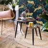 A cozy living room corner with a rattan chair, two nesting coffee tables, and a vibrant leopard-print wallpaper. Náhled obrázku produktu