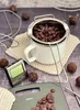 A collection of chocolate-making tools and ingredients, including a digital thermometer, a double boiler insert, chocolate chips, and chocolate truffles, arranged on a textured surface. Anteprima dell’immagine prodotto