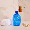 A shampoo bottle and a rolled towel are displayed on a marble-like surface, with a soap dispenser in the background. Anteprima dell’immagine prodotto