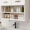 A white bathroom cabinet with shelves filled with various toiletries and bottles, mounted above a sink with a black faucet. Náhled obrázku produktu