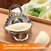 A stainless steel dumpling maker with dough inside, placed on a wooden surface, with finished dumplings in the background. Produktbild-Vorschau