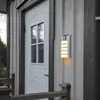 A solar-powered LED wall light mounted on the exterior wall of a house next to a white door. Podgląd zdjęcia produktu