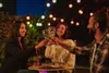 Three people are toasting with wine glasses at night, with string lights in the background. Náhled obrázku produktu