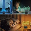A collage of three images showing a 3D game controller lamp in different settings: near a window with a child looking out, next to a child reading, and on a nightstand next to a sleeping child. Produktbild-Vorschau