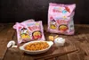 Two bags of Samyang Buldak Hot Chicken Carbonara Ramen and a bowl of prepared ramen are displayed on a wooden table. Produktbild-Vorschau