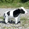A plush toy cow stands on a gravel path with grass in the background. Náhľad obrázku produktu