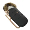 A black winter footmuff with a fur-lined hood is placed on a wooden sled. Podgląd zdjęcia produktu