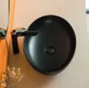 A black ceramic washbasin with a chrome faucet is shown on a light beige wooden surface, with an orange element and dried plants in the foreground. Náhľad obrázku produktu