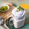 A close-up of a dessert drink with whipped cream and pistachios, served in a mason jar, with cookies and a bowl of pistachios on the side. Produktbild-Vorschau