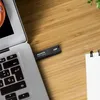 A black ADATA SSD USB flash drive is plugged into a silver laptop on a wooden desk. Anteprima dell’immagine prodotto