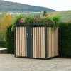 A trash bin enclosure with a green roof is situated outdoors on a paved patio, with a hedge and a hillside in the background. Produktbild-Vorschau