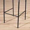 Close-up of the black metal legs of a bar stool on a wooden floor. Produktbild-Vorschau