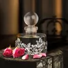A perfume bottle with decorative silver leaf accents, placed on a wooden surface with pink roses and petals. Voir les images du produit