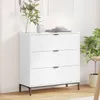A white dresser with three drawers is shown in a room with a plant and artwork in the background. Náhled obrázku produktu