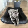 A French bulldog lies on a black dog bed in a room with wooden floors. Produktbild-Vorschau