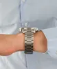 A close-up shot of a man's wrist wearing a silver watch. Produktbild-Vorschau