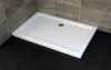A white rectangular shower tray is shown in a bathroom setting with dark tiled flooring and beige tiled walls. Produktbild-Vorschau