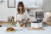 A woman is pouring fries from an air fryer basket into a bowl in a kitchen. Produktbild-Vorschau