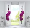 Two white panel curtains with purple orchid prints are displayed in a room with a large window showing a green outdoor scene.