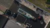 An aerial view of a truck with a trailer carrying various items, parked in a lot next to a building and a road. Náhled obrázku produktu
