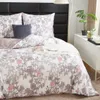 A neatly made bed with a floral pattern duvet cover and pillows, set against a black headboard, with a dresser and plant in the background. Podgląd zdjęcia produktu