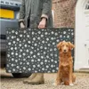 A person is holding a dog bed next to a car, with a dog sitting in front of the bed. Produktbild-Vorschau