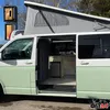 A camper van with its side door open, showing the interior setup and a pop-top roof extended. Voir les images du produit