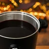 A close-up of a black mulled wine cooker filled with red liquid, with blurred bokeh lights in the background. Produktbild-Vorschau